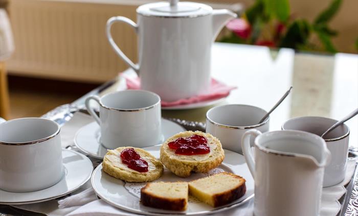 Afternoon tea;teapot, two cups sugar b owls, milk jug, scones and lemon drizzle cake.